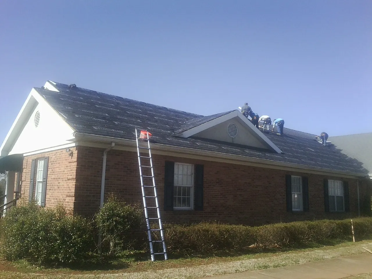 Crew tearing shingles off a brick ranch roof with a ladder set — Metal Roof Repair work by our crew in Commerce