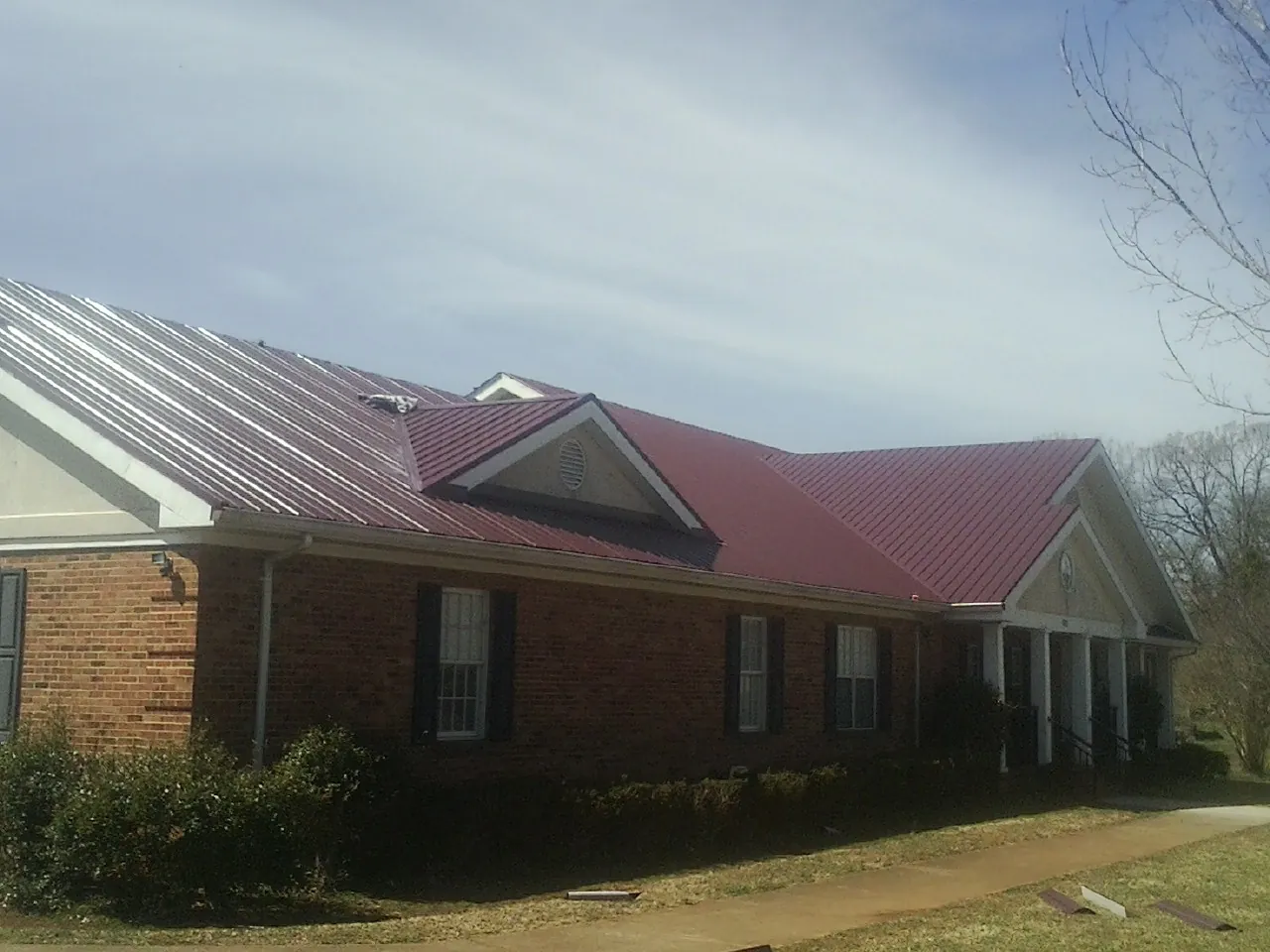 Red metal roof with gabled entries on a long brick building, from a Hail Damage Roof Repair job in Commerce