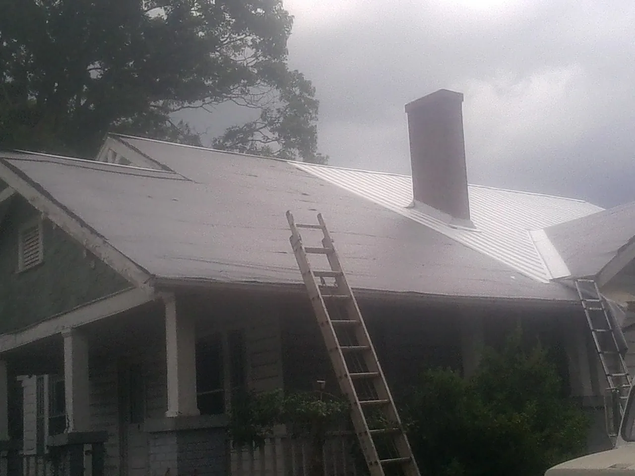 Ladders against a metal roof on an older home with a brick chimney in Commerce