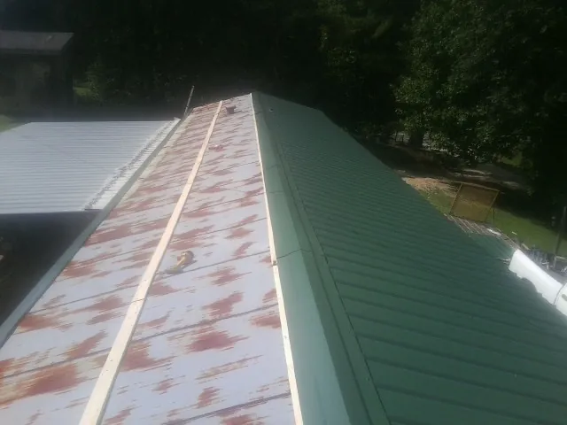 Old rusted panels beside newly installed green metal roofing — Wind Damage Roof Repair by Roofing Brothers in Commerce