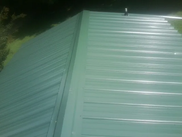 New green metal panels meeting at the ridge of a roof — Flat Roof Repair work by our crew in Commerce